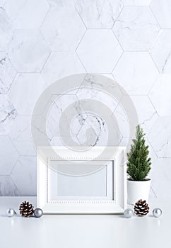 White vintage photo frame with christmas tree,pine cone and decor xmas ball on white table and marble tile wall background.clean