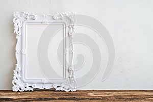 White vintage photo frame on old wooden table over white wall ba