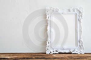 White vintage photo frame on old wooden table over white wall ba