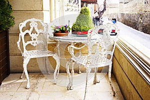 White vintage wrought iron gardening furniture, set of empty round table and two elegant chairs on balcony.