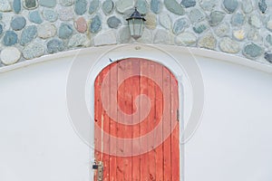 White wall decorated with stones, street lantern over red wooden door