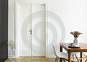 A white wall with double door next to a wooden breakfast table and chairs in a dining room interior. Real photo.