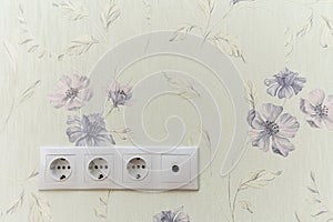 A white wall with a floral pattern and a white electrical outlet