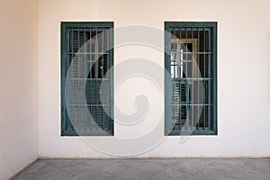 White wall with grunge windows with wooden green shutters and wrought iron bars and marble floor