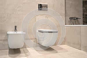 White wall-hung bidet and toilet, on gray ceramic tiles in bathroom