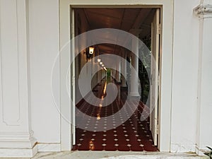 white walls with doors opening into a hallway lined with pillars and wall lamps. patterned red tile floors