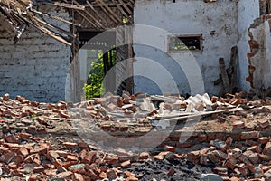 The white walls of an old ruined wooden village house. Broken walls, a ruined roof. Piles of garbage, wooden boards