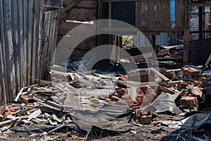 The white walls of an old ruined wooden village house. Broken walls, a ruined roof. Piles of garbage, wooden boards