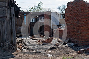 The white walls of an old ruined wooden village house. Broken walls, a ruined roof. Piles of garbage, wooden boards