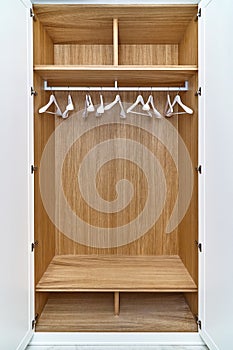 White wardrobe with wooden drawers and shelves. Wooden filling of wardrobe and white clothes hangers