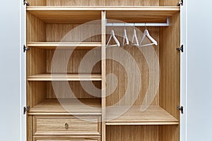 White wardrobe with wooden drawers and shelves. Wooden filling of wardrobe and white clothes hangers