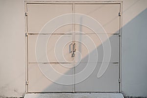 White warehouse metal steel gate with locker locked in sunset light and shadow. symmetric factory door closed with lock.