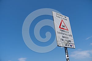 White warning sign alerting for the danger of falling in the sea on a blue sky background photo