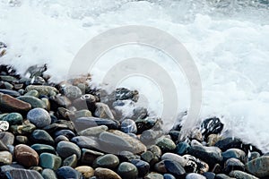 White wave washing the stones of the shore. Background with beach of stone.