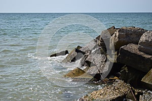 White waves breaking on sandy beach through gap in rocks on sea. Rock fragments on a wild beach
