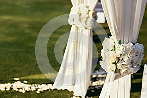 White wedding arch with flowers on sunny day in ceremony place