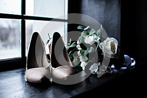 White wedding bouquet and pink shoes of the bride near the window