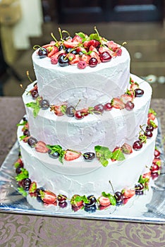 White wedding cake decorated by flowers fruits