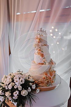 A white wedding cake, decorated with flowers and gold, stands on a glass stand.