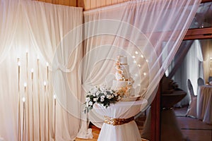 A white wedding cake, decorated with flowers and gold, stands on a glass stand.