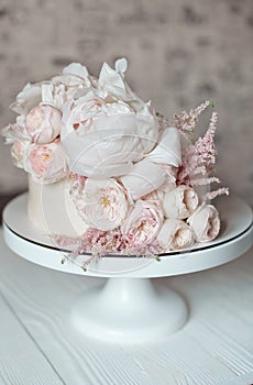 White wedding cake decorated with fresh roses, peonies and greenery