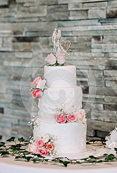 White wedding cake decorated with red roses and figurine in the shape of a bride and groom