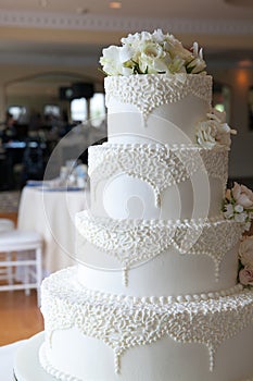 White wedding cake with white flowers and fancy designs with a reception hall in the background photo