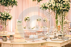 WHITE  WEDDING CAKE AT IMPRESSIVE COLOURFUL VENUE WITH BEAUTIFUL CANDY TABLES, FLORAL GREEN DECORATION, BLURRED BACKGROUND, YELLOW