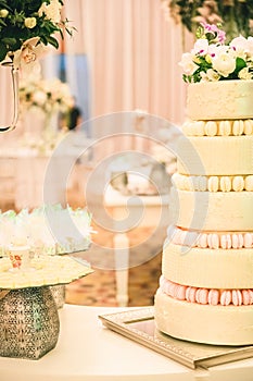 WHITE  WEDDING CAKE AT IMPRESSIVE COLOURFUL VENUE WITH BEAUTIFUL CANDY TABLES, FLORAL GREEN DECORATION, BLURRED BACKGROUND, YELLOW