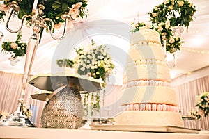 WHITE  WEDDING CAKE AT IMPRESSIVE VIOLET VENUE WITH BEAUTIFUL CANDY TABLES, FLORAL GREEN DECORATION, BLURRED BACKGROUND, YELLOW LI