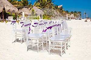 White wedding chairs decorated with purple bows on