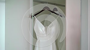 A white wedding dress on a hanger in a room. Morning of the bride.