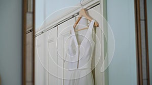 A white wedding dress on a hanger in a room. Morning of the bride.