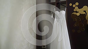 A white wedding dress on a hanger in a room. Morning of the bride.