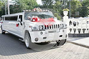 White wedding limousine decorated with red ribbons, wedding rings and flowers. Wedding concept.