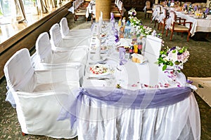 White wedding party table with fancy chairs and a lot of flowers, decorations, beverages and plates with food