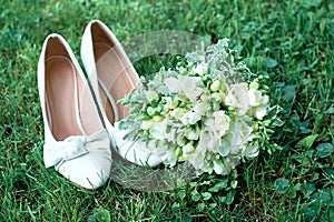 White wedding shoes on green grass. Beautiful bridal bouquet and snow-white freesias