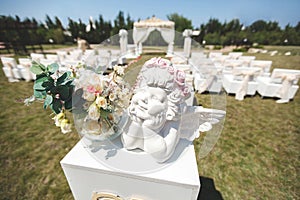 White wedding tent for the ceremony outdoors. Arch. Chairs. The figure of an angel in plaster.