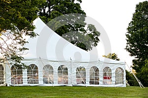 A white wedding tent set up in a lawn surrounded by trees and with the sides down photo