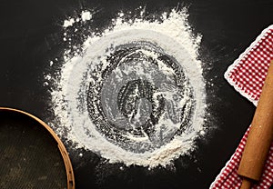 White wheat flour scattered on a black table and very old brown wooden rolling pin