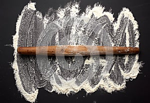 White wheat flour scattered on a black table and very old brown wooden rolling pin on a black table