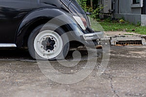 White wheel with Tire leak of the black old car. It parked on the cement road.