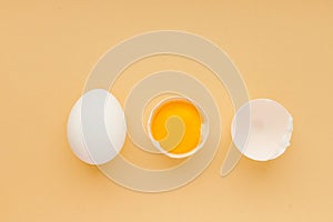 White whole chicken egg , yolk and empty cracked eggshell on yellow background, top view.