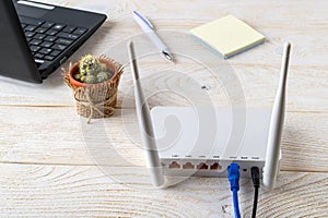 White Wi-Fi wireless router near laptop on a white wooden table. Wlan router with internet cables plugged in on a table in a home