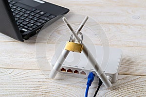 White Wi-Fi wireless router with padlock on antennas near laptop over white wooden table. Forbidden or limited internet and