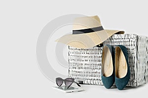 White wicker suitcase, womens hat, sunglasses, blue shoes and e-book.