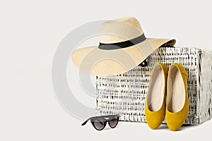 White wicker suitcase, womens hat, sunglasses and yellow shoes.