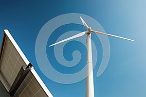 White windmill and solar panel for energy generation stands on farm