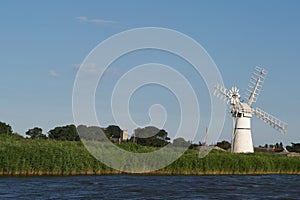 White windmill wind pump on a summer riverbank