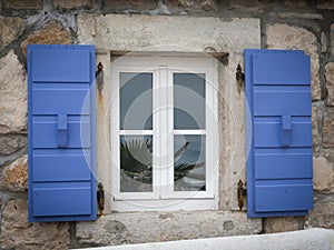 A white window with blue shutters, reflection of plants